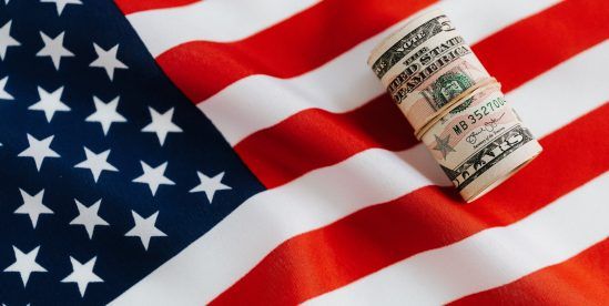 From above of United States currency folded in roll placed on USA flag illustrating concept of business profit and wealth